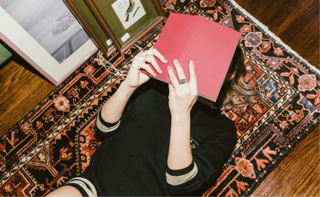 woman laying on ground reading red book